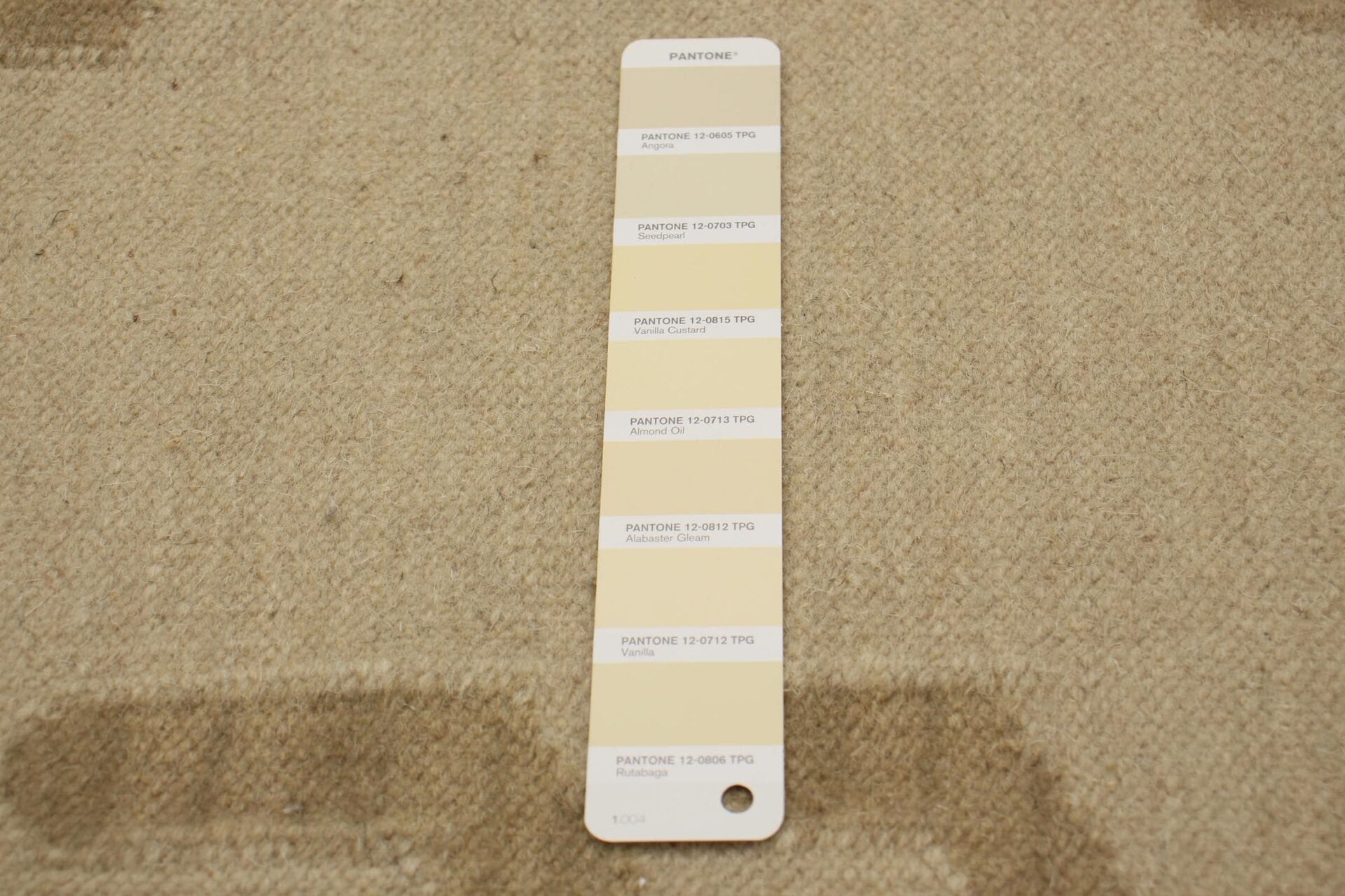 Een Pantone-kleurenmonsterkaart met verschillende tinten en labels wordt elegant op een beige structuurvloerkleed geplaatst.