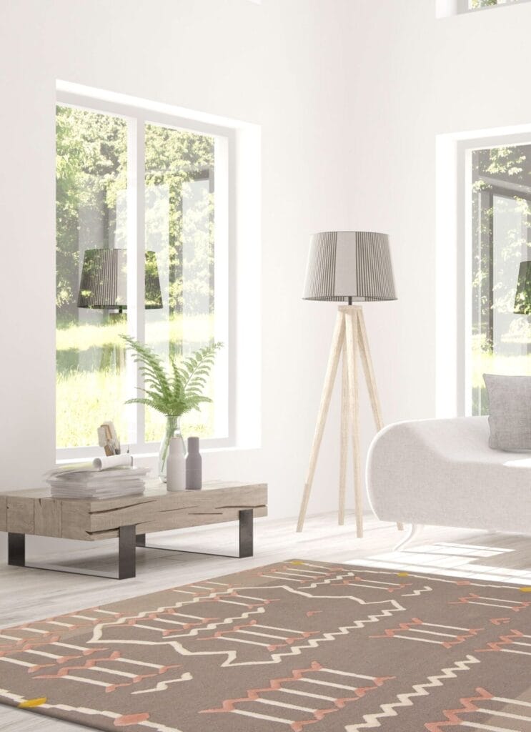 Moderne woonkamer met grote ramen, een tapijt met patroon, een witte bank, een hoge staande lamp en een houten salontafel met boeken en een plant in een vaas.