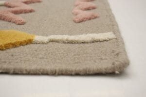 Close-up van een geweven tapijt in beige en roze met een geometrisch patroon, bekeken vanaf de rand op een glad oppervlak.