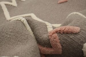 Close-up van een structuurstof met een zigzagpatroon in beige en lichtroze op een bruine achtergrond.
