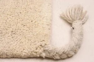 Close-up van de hoek van een beige, donzig vloerkleed met een gevlochten pony die eindigt in een plukje.