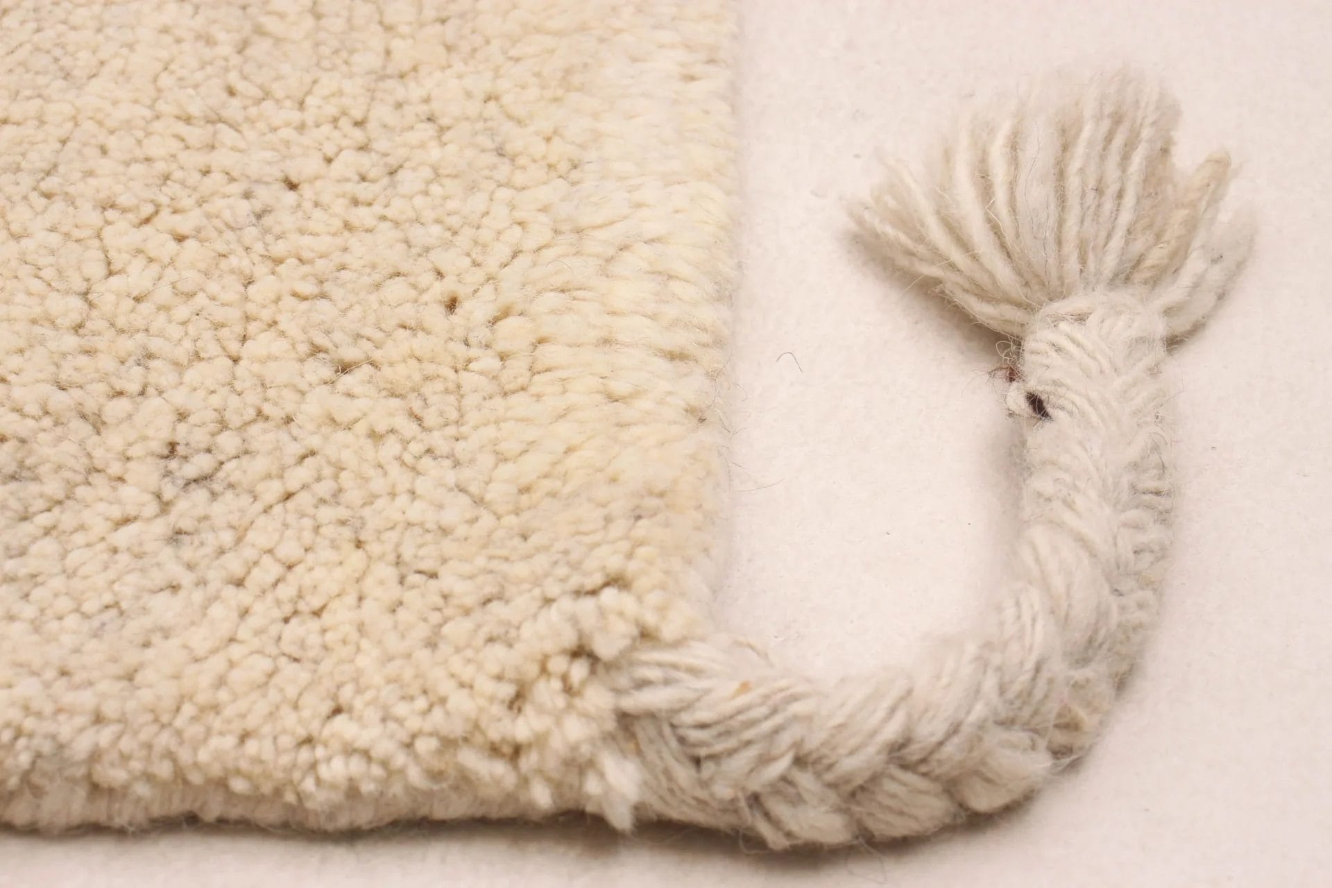 Close-up van de hoek van een beige, donzig vloerkleed met een gevlochten pony die eindigt in een plukje.