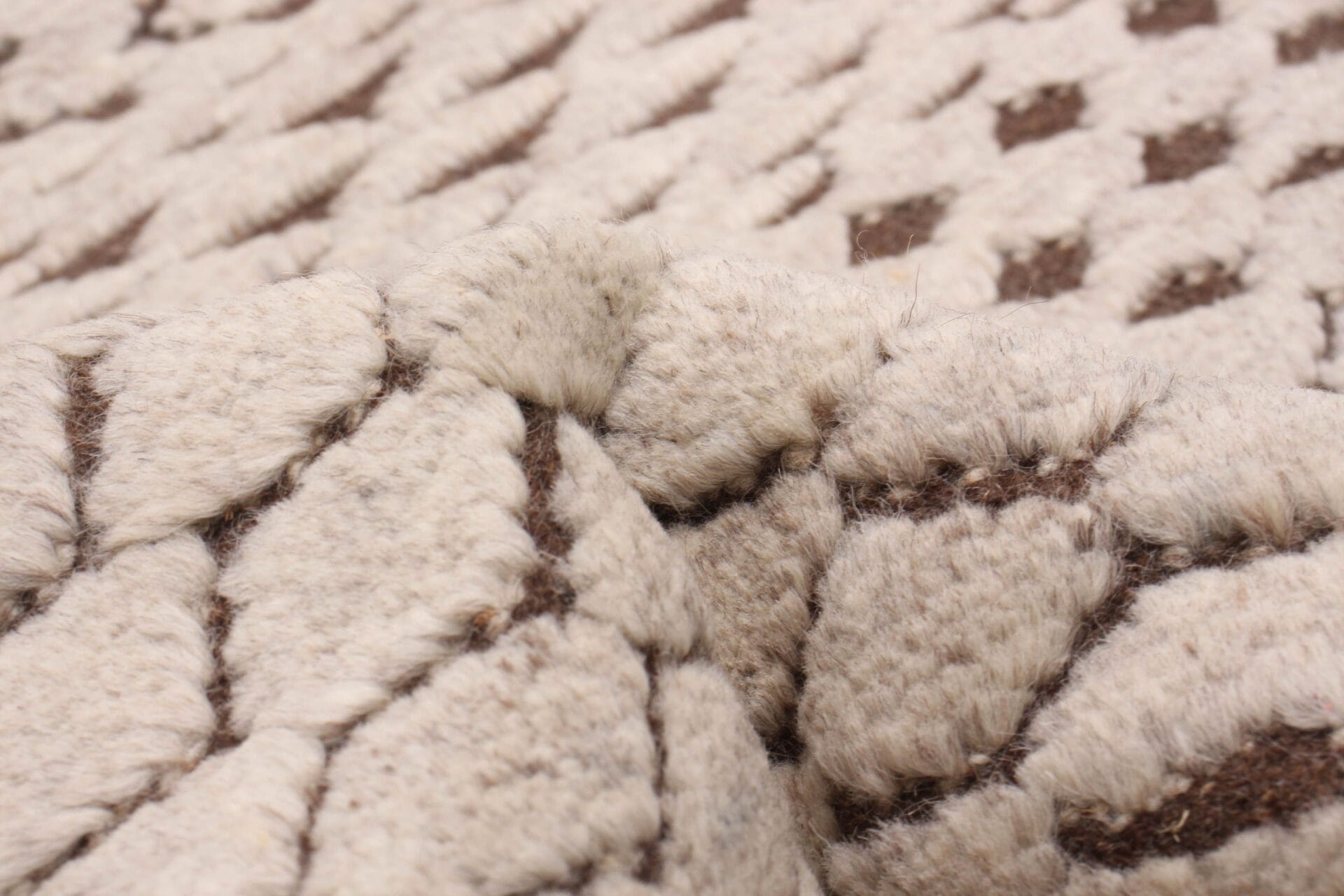 Close-up van een vloerkleed met een beige en bruin patroon en een verhoogd, gestructureerd oppervlak, met gedetailleerde stiksels en een zachte, donzige textuur.