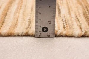 Een liniaal staat verticaal op een beige, gestructureerd tapijt en meet een hoogte van ongeveer 0,5 centimeter.