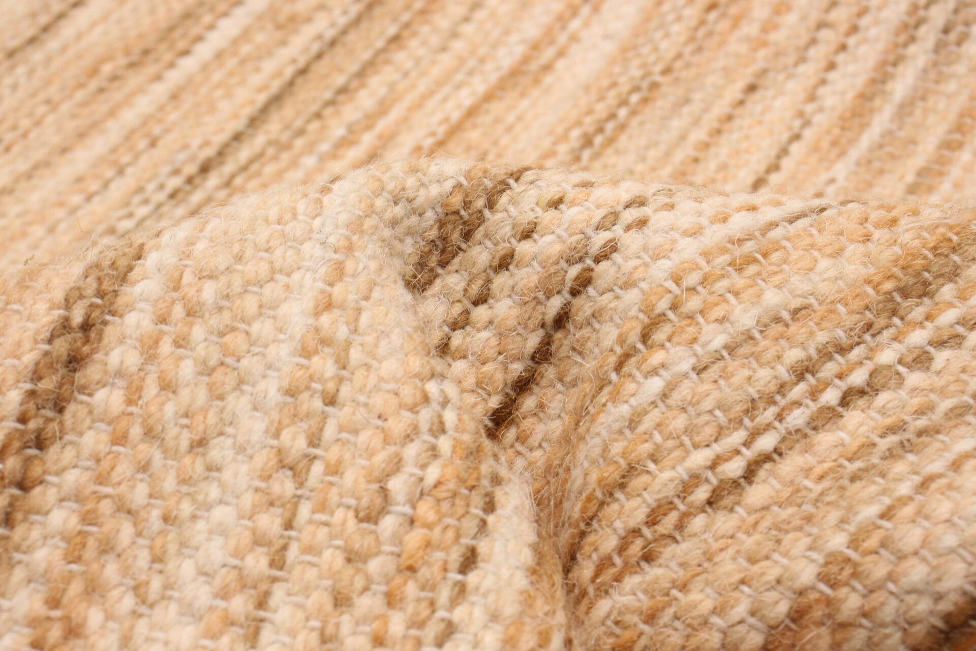 Close-up van een getextureerde, beige gebreide stof met subtiele variaties in kleur en steekpatroon, die lijkt op de ingewikkelde details van een geweven tapijt.