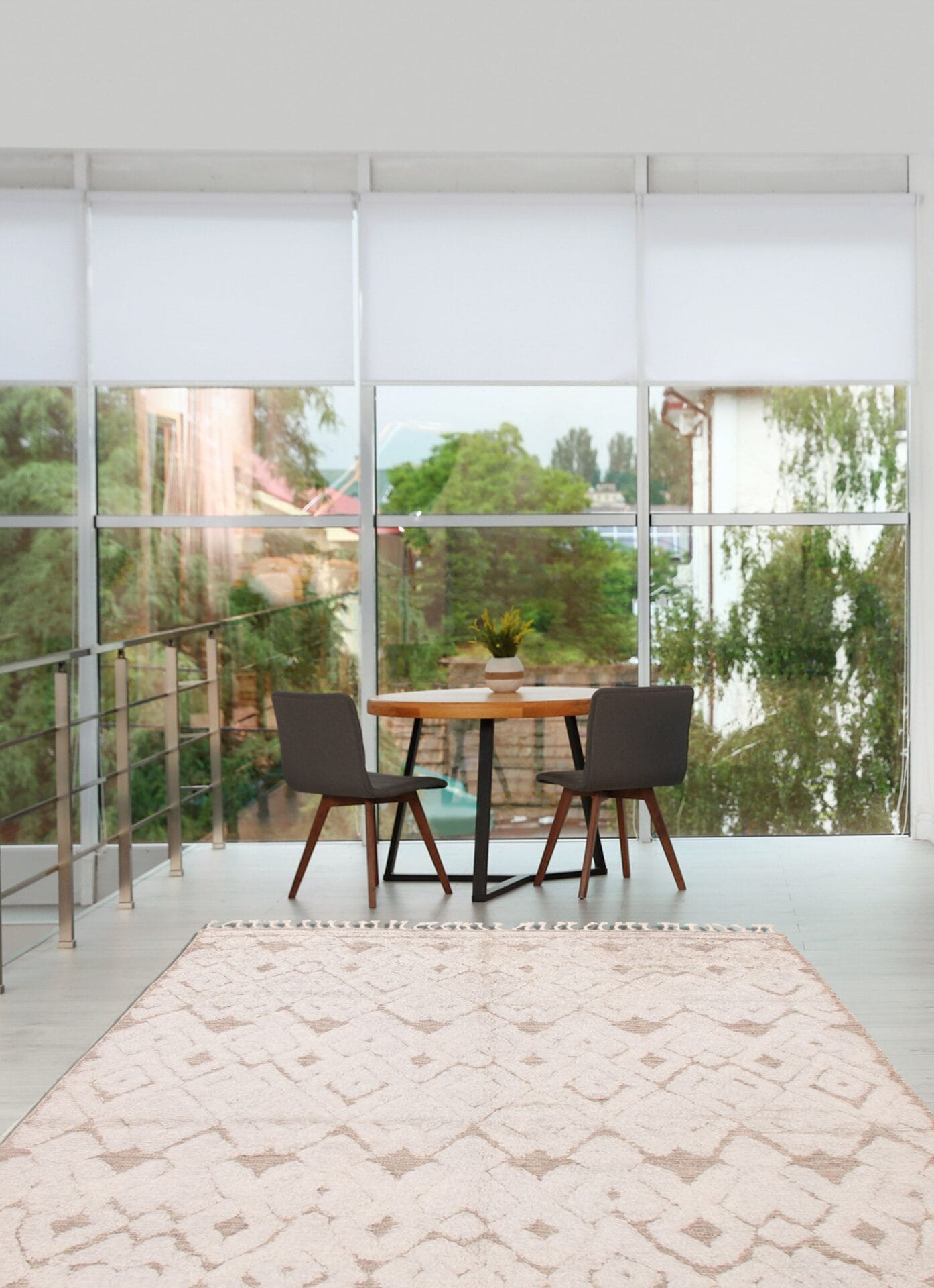 Kleine eethoek met een houten tafel en twee grijze stoelen voor kamerhoge ramen met uitzicht op het groen. Een vloerkleed met beige patroon bedekt de vloer.