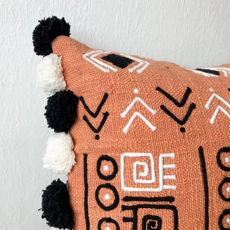 Close-up van een decoratief kussen met zwart-witte geometrische patronen, versierd met zwart-witte pompons op de hoeken.