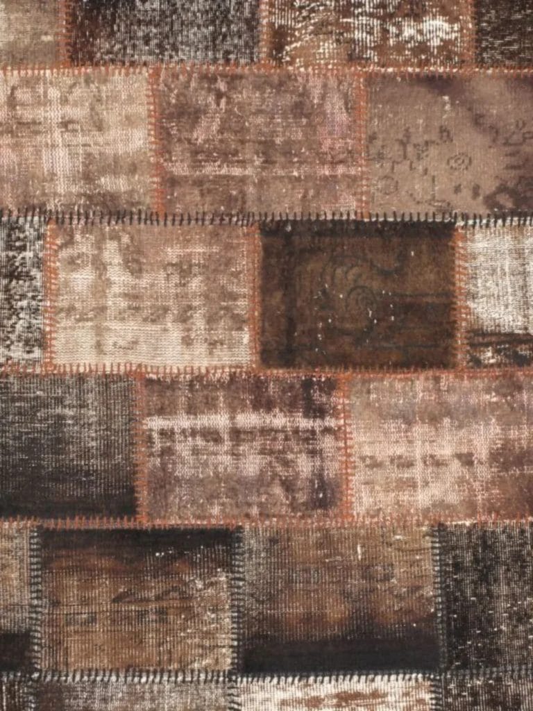 Een patchwork-kleed met verschillende rechthoekige stukken stof in de kleuren bruin, beige en lichtbruin, die in een ordelijk patroon aan elkaar zijn gestikt.
