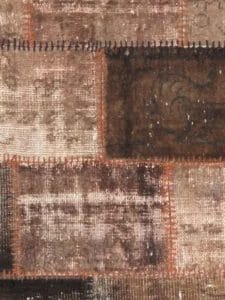 Close-up van een patchworkstof met gestikte rechthoekige stukken in verschillende tinten bruin en beige, met gestructureerde en versleten oppervlakken.