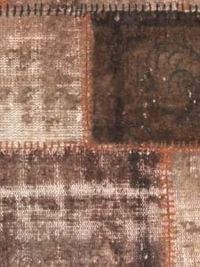 Close-up van een patchworkstof met vierkanten in verschillende tinten bruin en zichtbare stiksels.