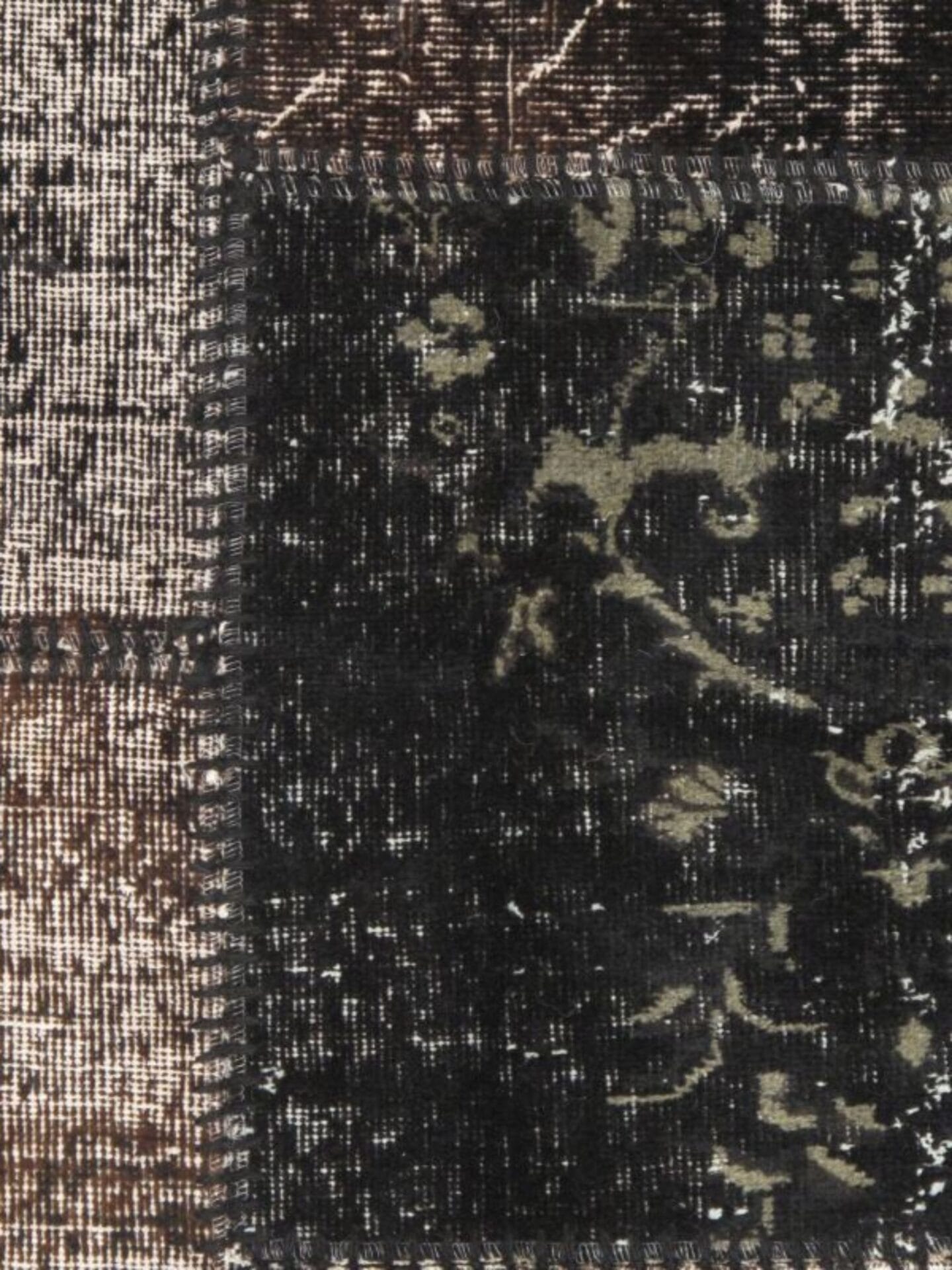Close-up van een patchwork textieltapijt met verschillende stoffen vierkanten in de kleuren zwart, grijs en bruin met verschillende texturen en patronen.