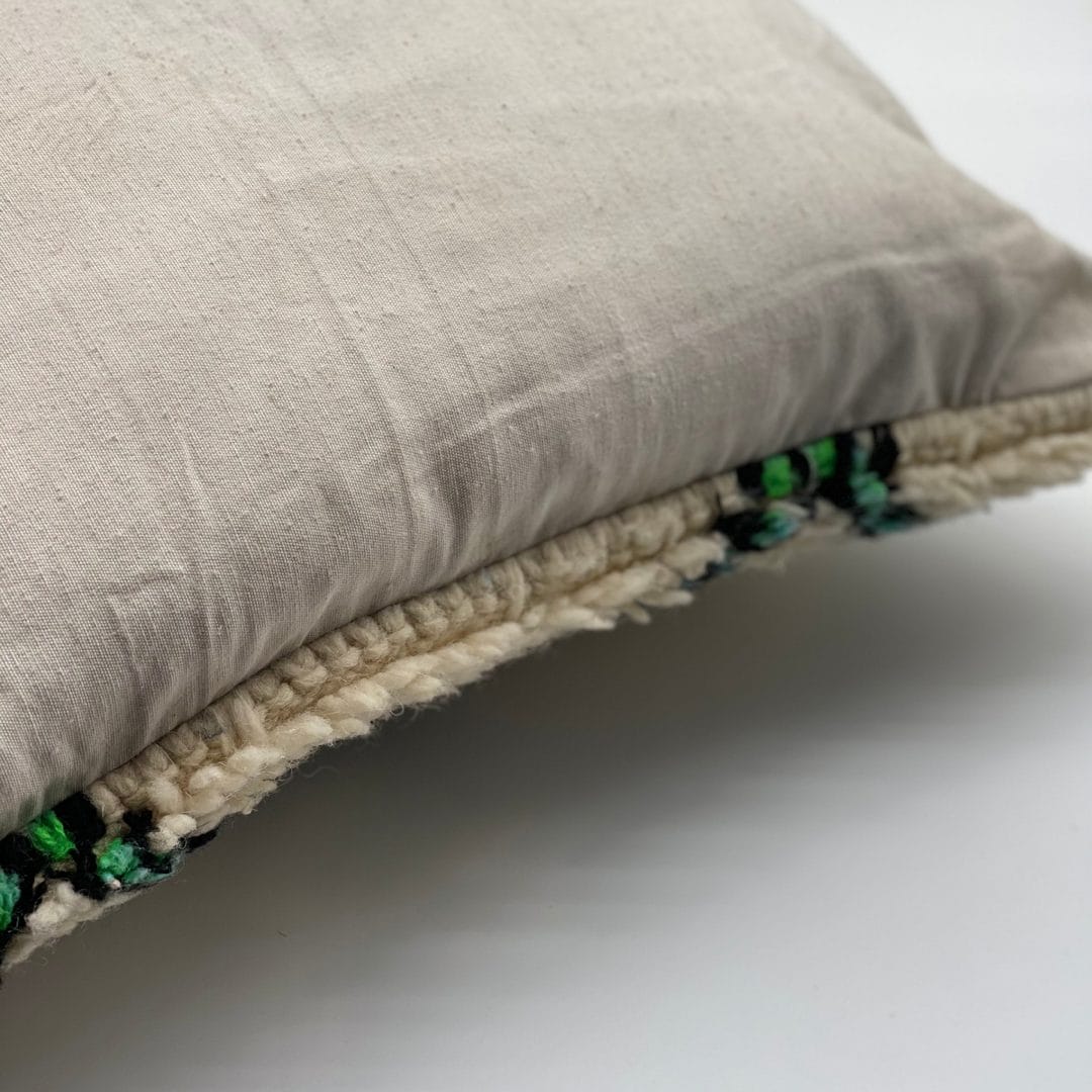 Een close-up van een beige kussen met een gestructureerde rand, met groene en donkere accenten.