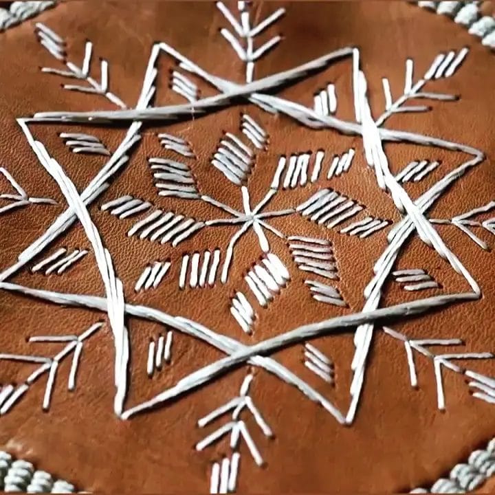 White geometric embroidery design on a brown leather background.