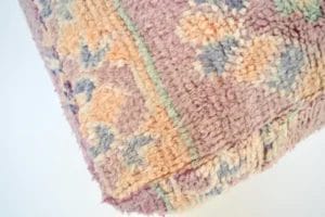 Close-up van een hoek van een veelkleurige, gestructureerde stof met een bloemenpatroon. De kleuren omvatten tinten roze, oranje, blauw en groen.