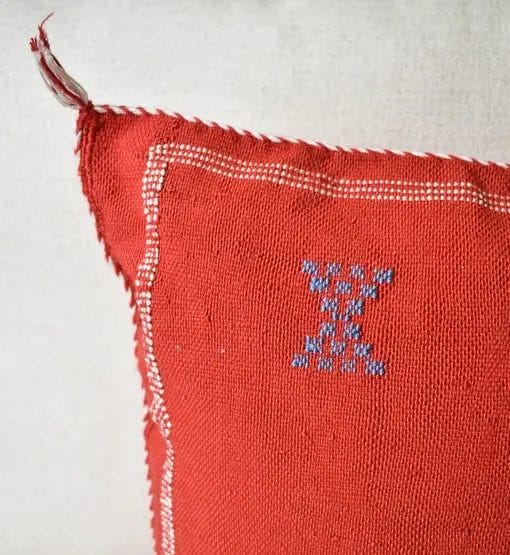 Rood kussen met witte randen en een klein blauw kruissteekpatroon in de hoek.