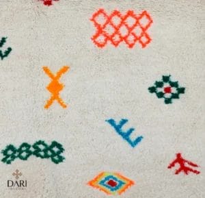Een crèmekleurig textiel met geometrische patronen in fel oranje, groen, rood en blauw. Het Dari Deco-logo is zichtbaar in de linkerbenedenhoek.