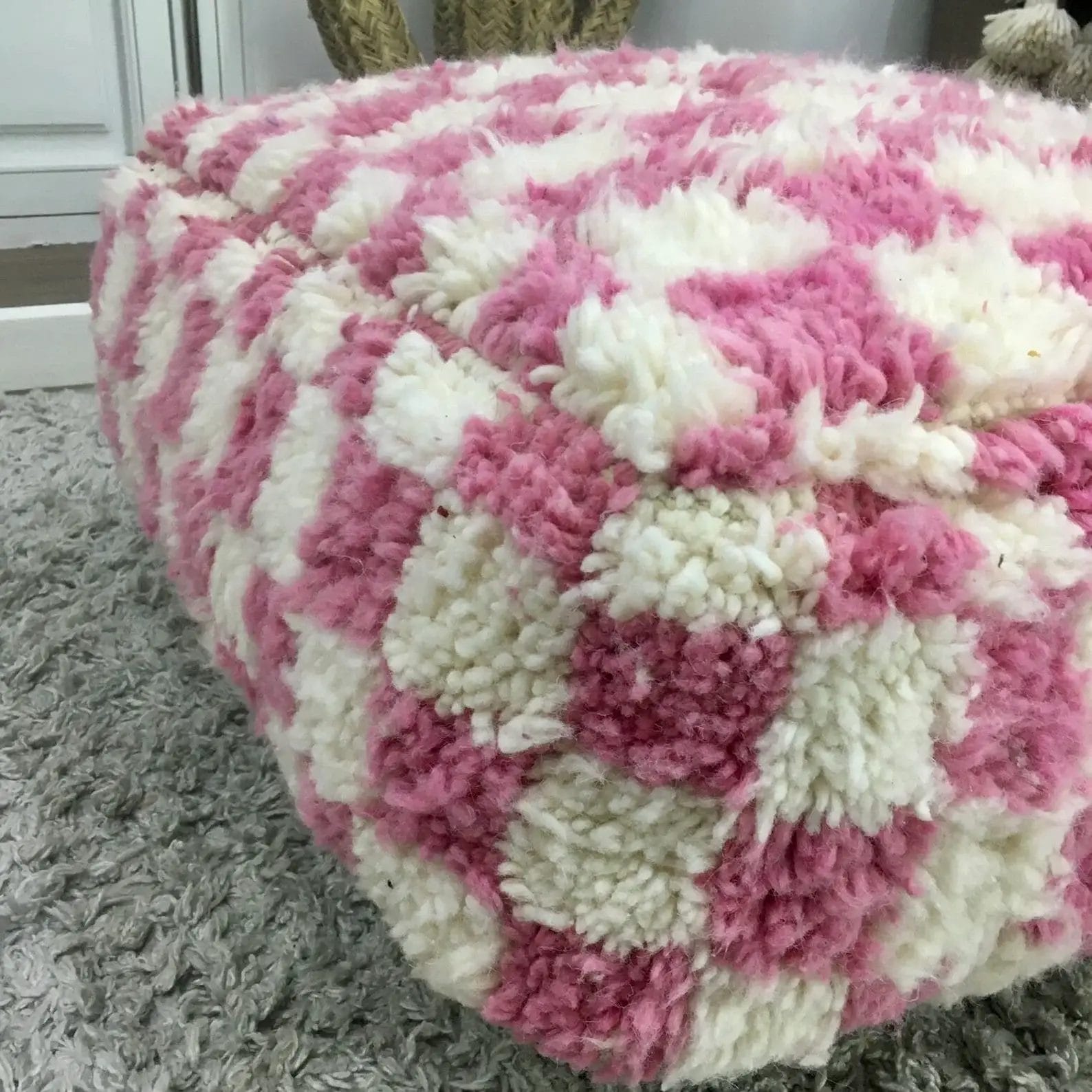 Een zachte roze en wit geblokte poef op een grijs tapijt.
