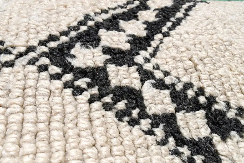 Close-up van een geweven tapijt met zwarte geometrische patronen op een crèmekleurige achtergrond.