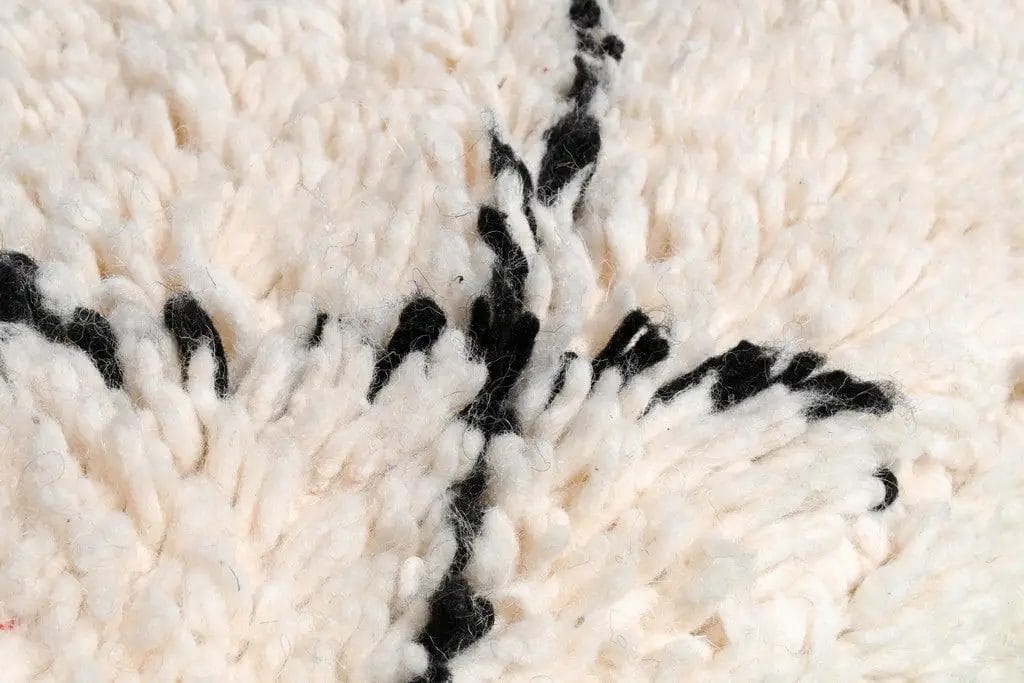 Close-up van een wollen tapijt met een structuur, waarbij witte en zwarte draden in een lineair patroon met elkaar verweven zijn.