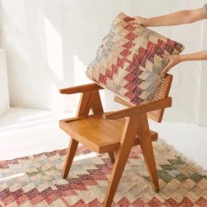 Handen leggen een Kussenhoes 50 x 50 cm | Arnav op een houten fauteuil met daaronder een bijpassend tapijt.