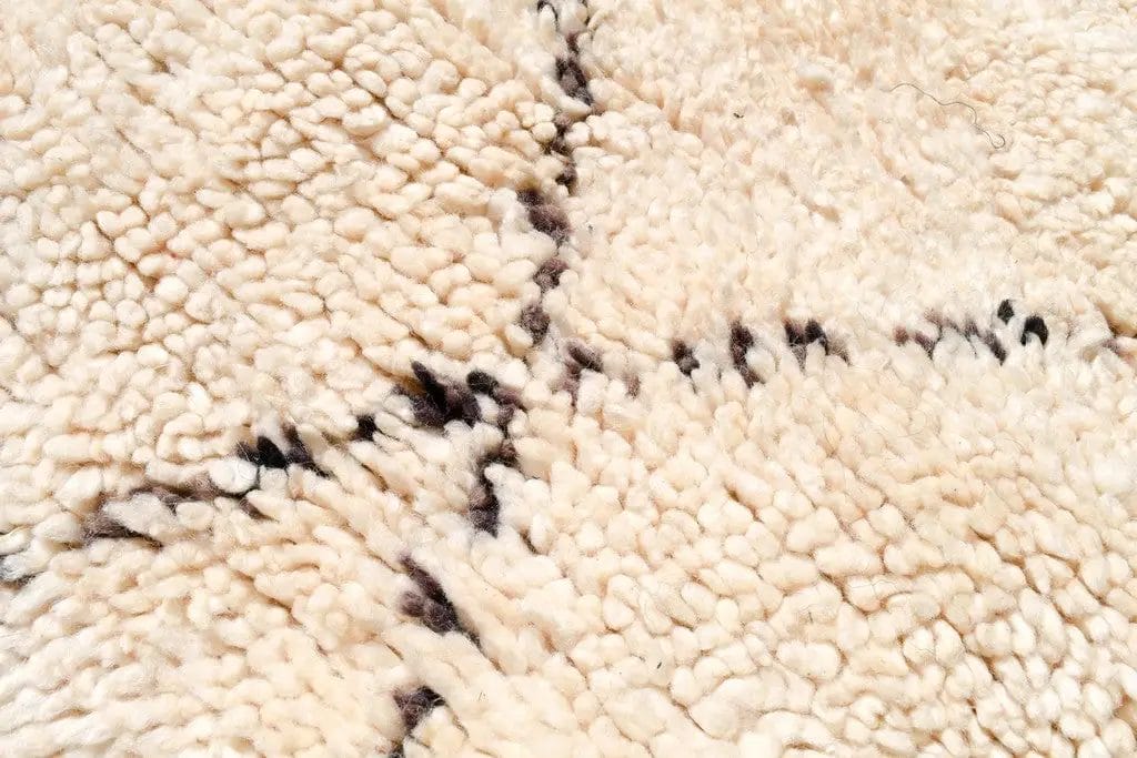 Close-up van een crèmekleurig shaggy tapijt met structuur en zwarte zigzagpatronen.