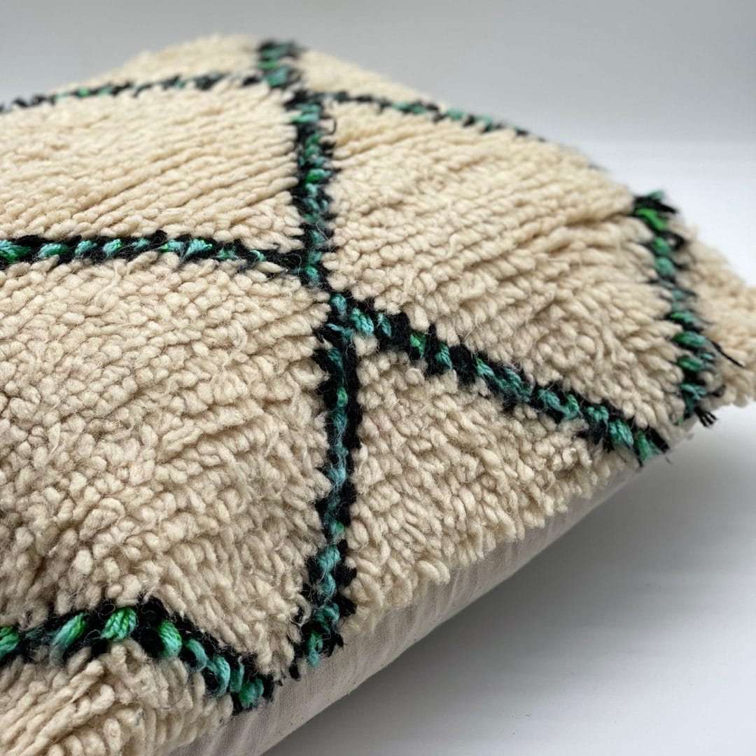 Een close-up van een beige kussen met een structuur en zwarte en groene kruispatronen.