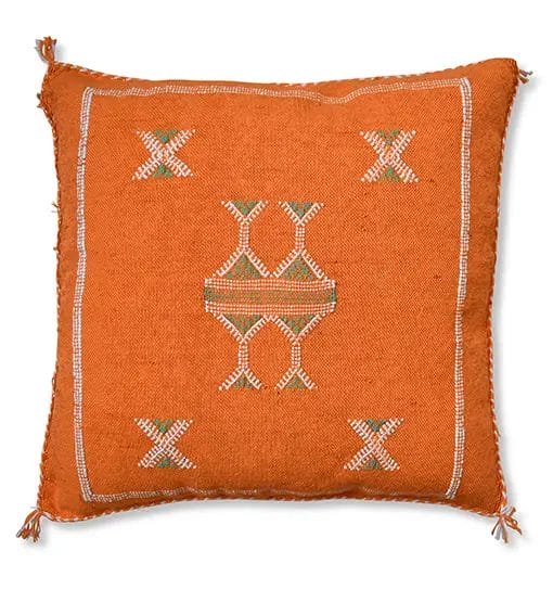 Het SABRA kussen van cactuszijde, kussen van Uksintas is een vierkant, oranje kussen versierd met symmetrische geometrische borduurpatronen in wit en groen. Met kwastjes op elke hoek. Het is een perfecte aanvulling op elk vloerkleed of tapijt in uw woonkamer.