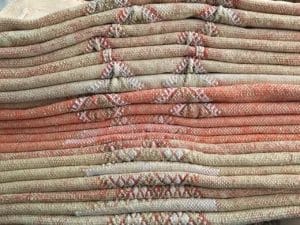 Een stapel gevouwen tapijten met patronen in oranje en beige tinten en geometrische patronen.