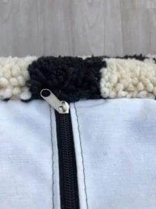 Close-up van een zwarte rits op een wit-zwarte structuurstof, met een licht houten oppervlak op de achtergrond.