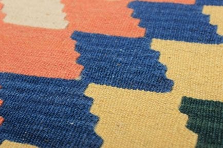 Close-up van een kleurrijke stof met zigzagpatronen in oranje, blauw, geel en groen.