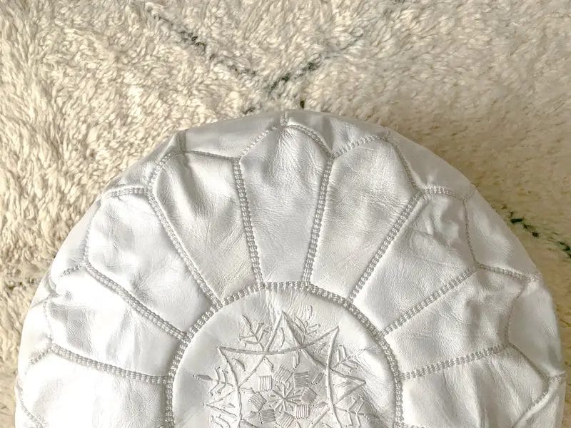 Wit rond kussen met bloemenborduursel op een beige oppervlak.