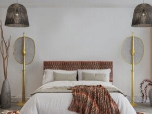 Een moderne slaapkamer met een groot bed, hoofdeinde met patroon, wit beddengoed, een kleurrijk vloerkleed en unieke gouden vloerlampen. Aan het plafond hangen twee hanglampen.