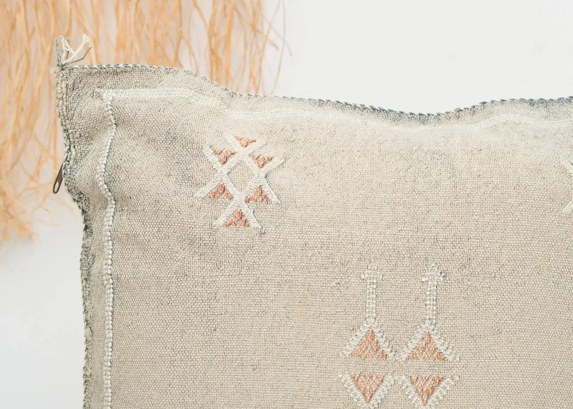 Een close-up van een beige kussen met textuur en geborduurde geometrische patronen in gedempte kleuren.