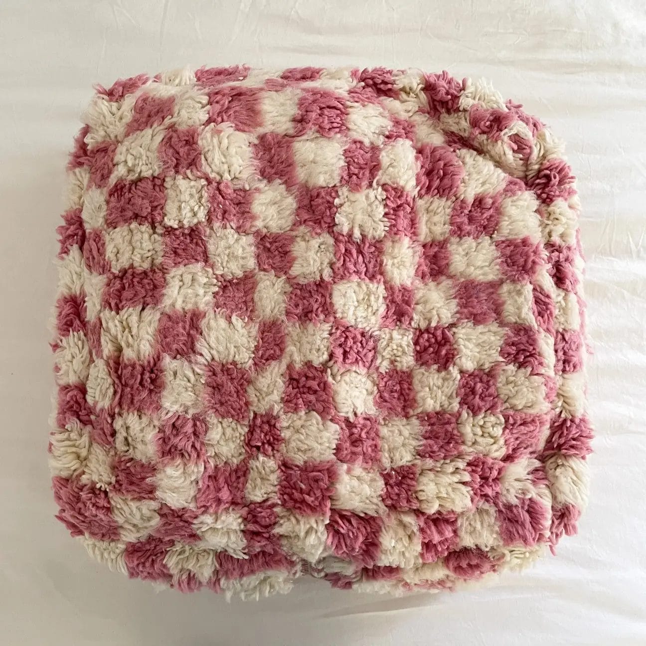 Een zachte, geruite deken in roze en wit ligt gevouwen op een wit oppervlak.