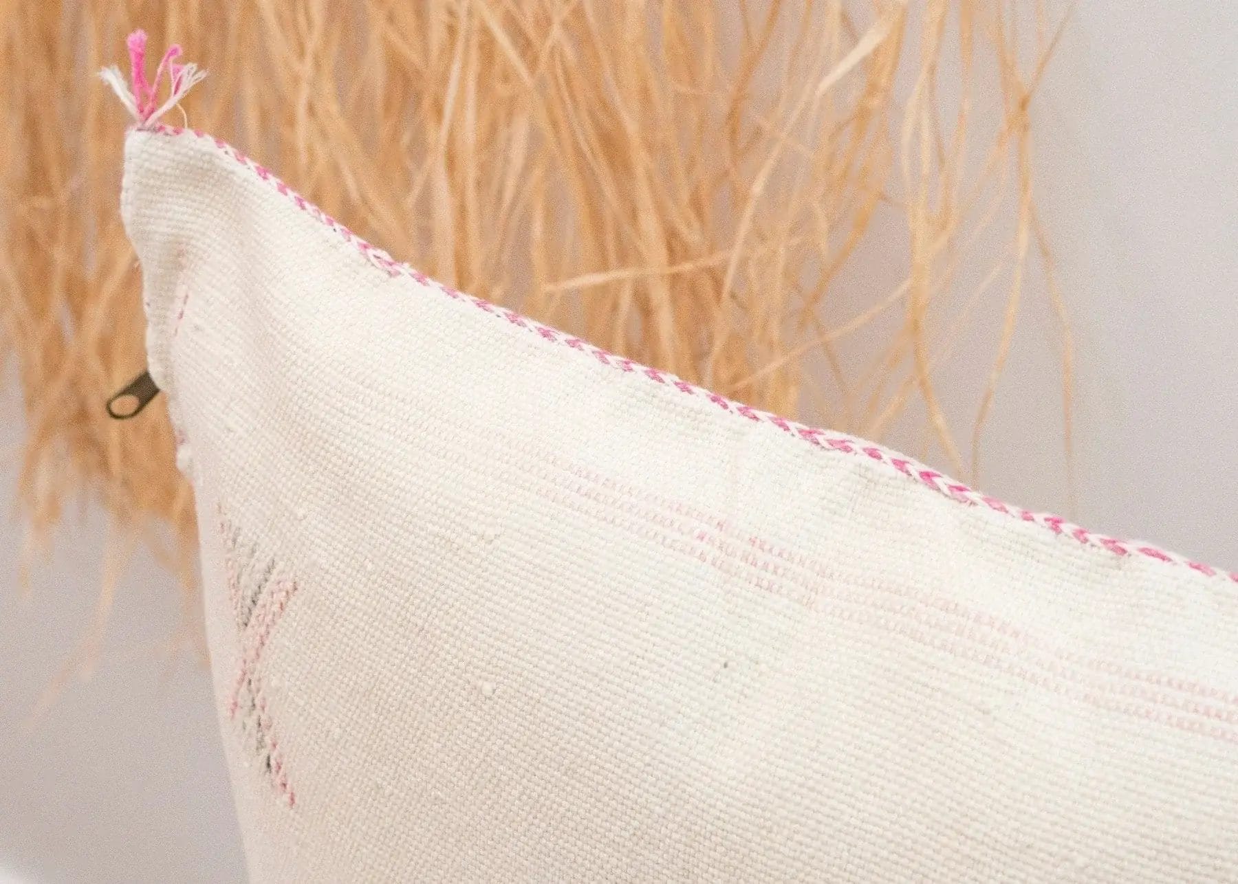 Close-up van een beige kussen met roze stiksels, tegen een achtergrond van gedroogd gras of stro.