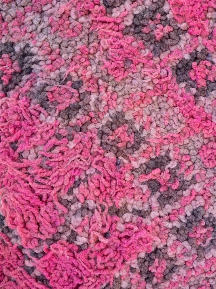 Close-up van een gestructureerde, veelkleurige stof met tinten roze en grijs in een lusvormig, wazig patroon.
