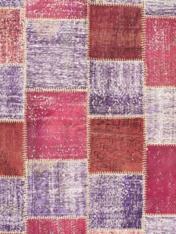 Een patchworkpatroon met rechthoekige lappen in de kleuren roze, paars en rood, met zichtbare stiksels.