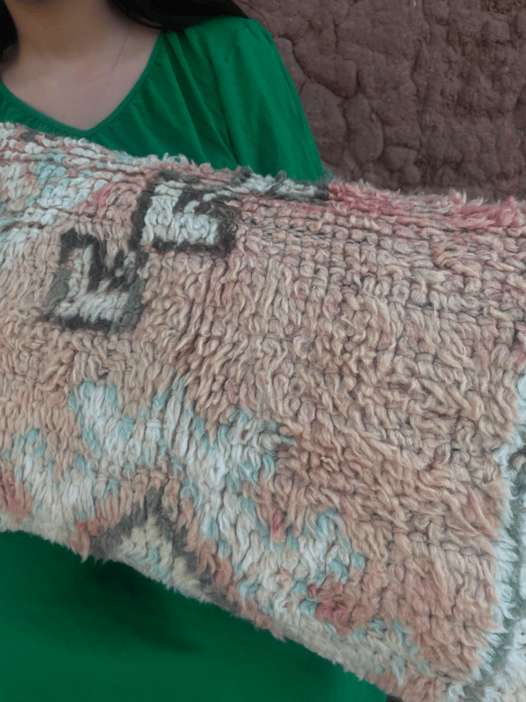 Persoon houdt een veelkleurig tapijt met textuur vast tegen een roze muur.