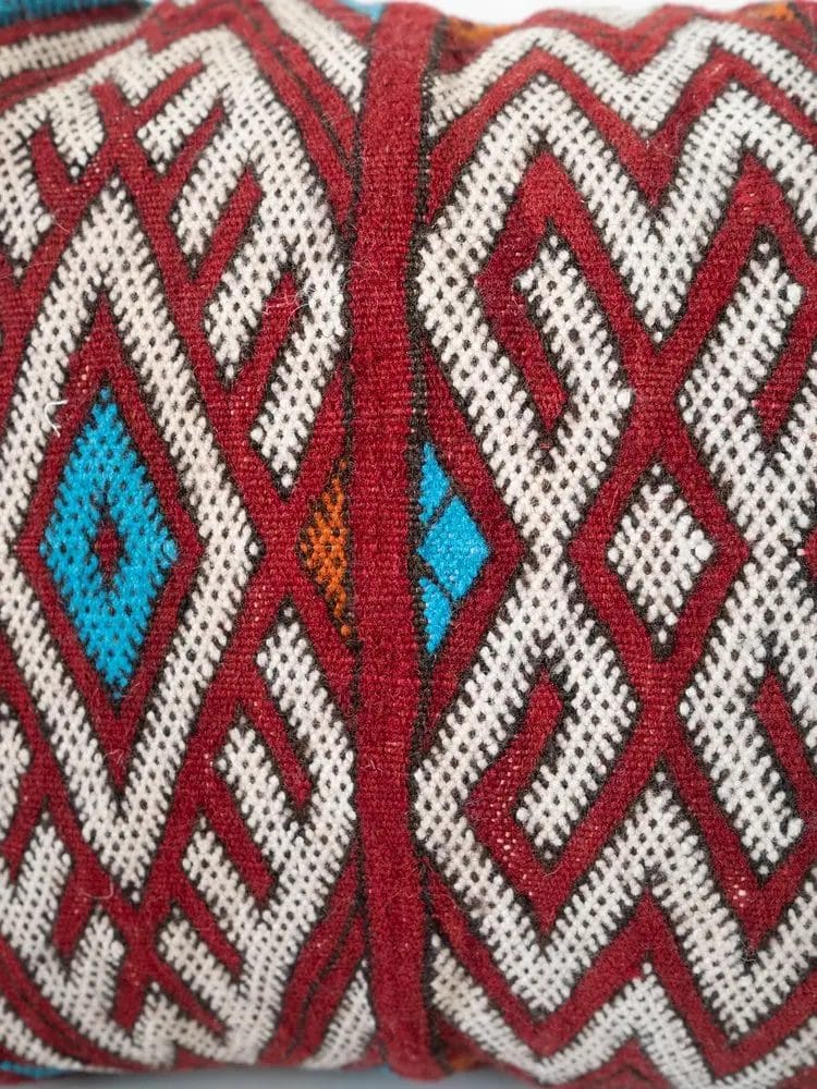 Close-up van een textiel met geometrische patronen in rood, wit, blauw en oranje. Het ontwerp bevat ruitvormen en ingewikkelde lijnen.