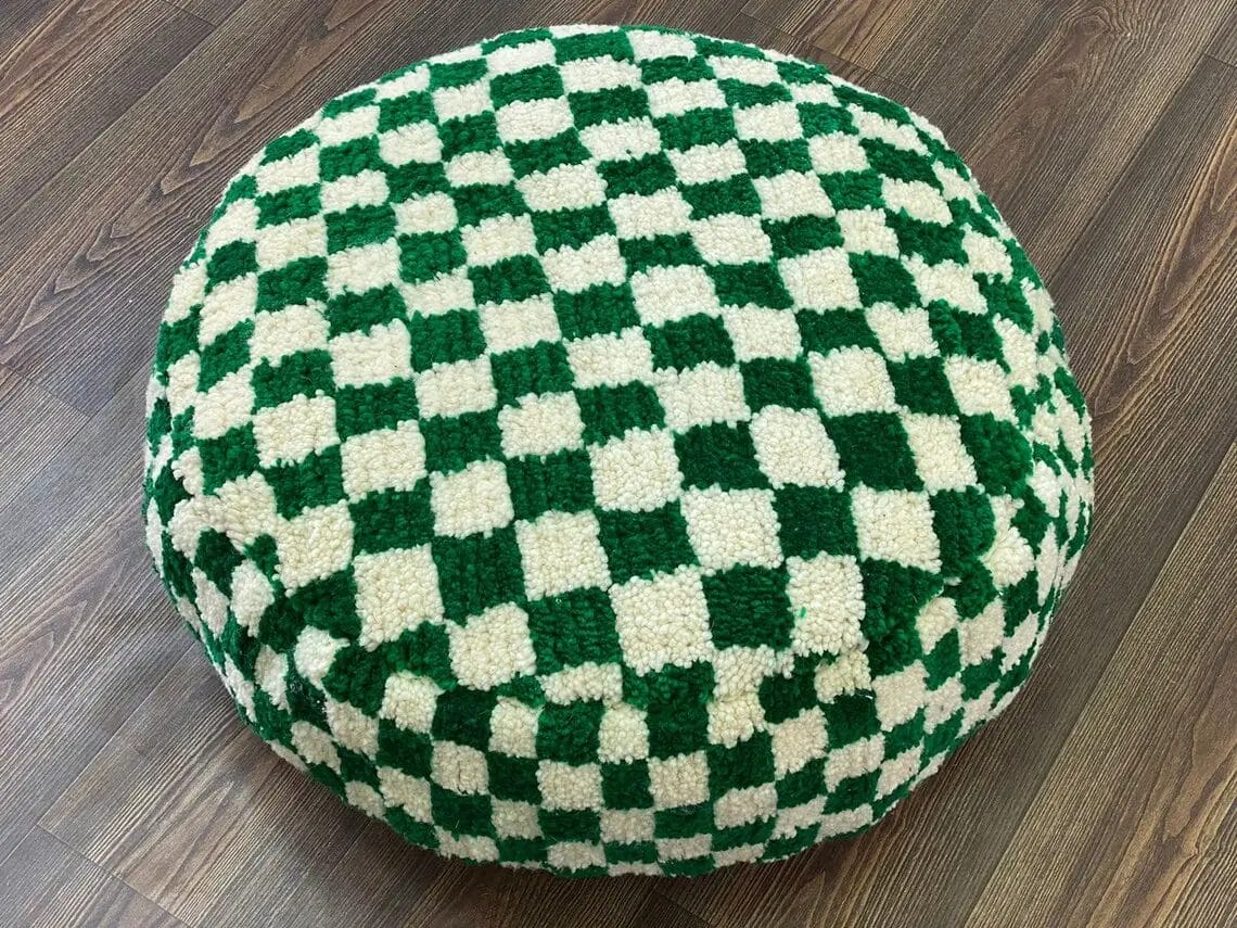 Ronde poef met een groen-wit schaakbordpatroon op een houten vloer.