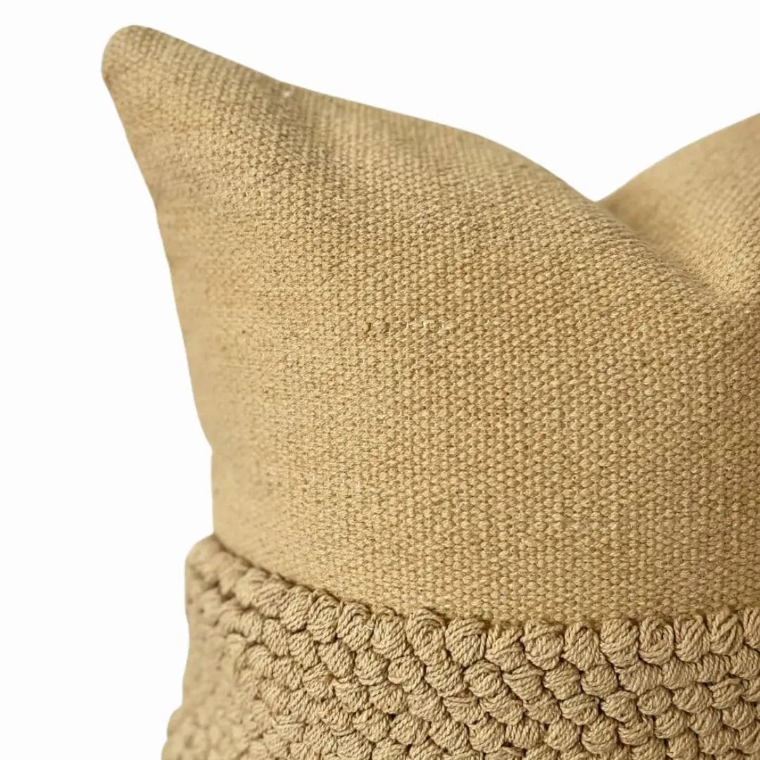 Close-up van een beige kussen met structuur en een gebreide band om het midden.