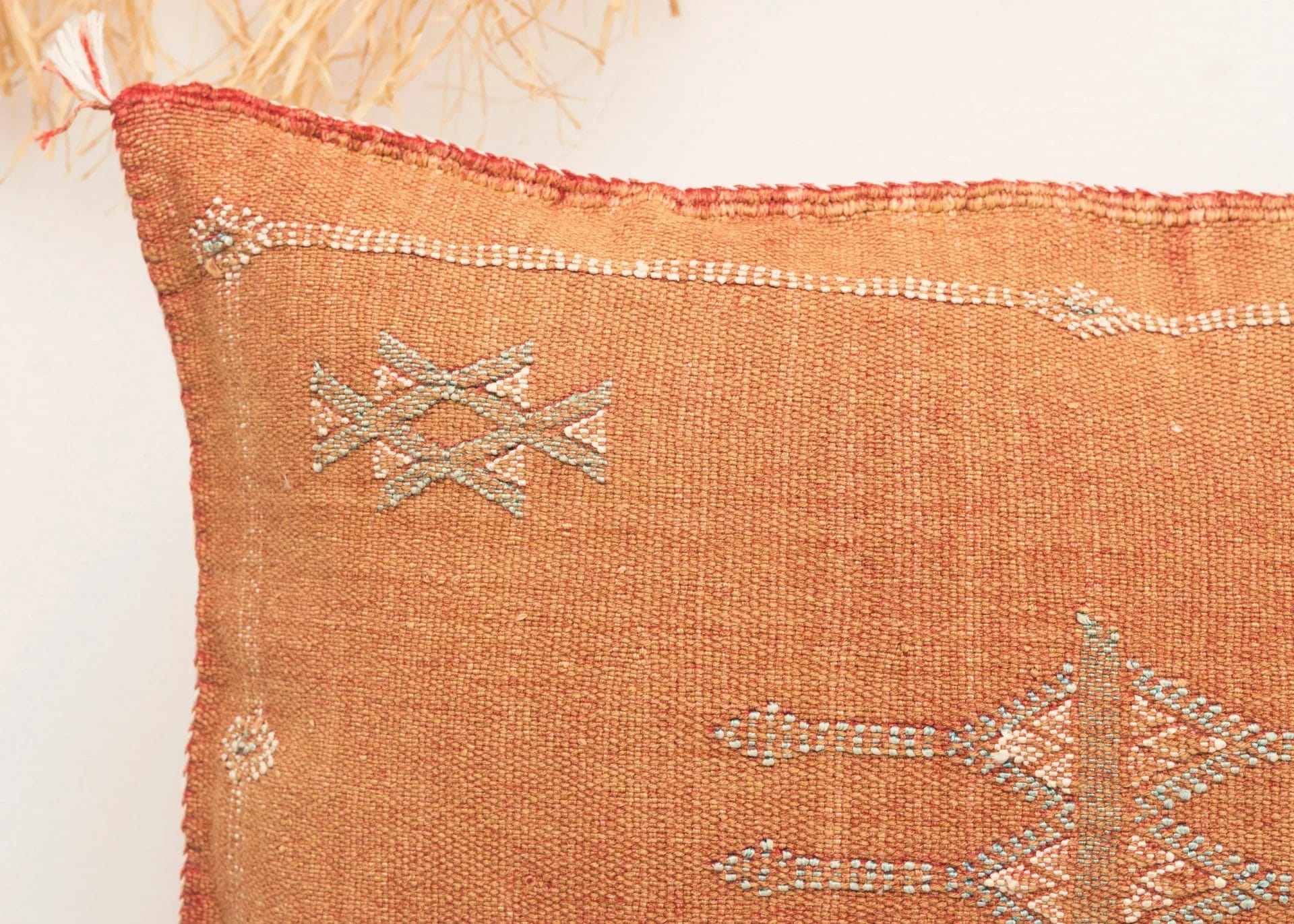 Close-up van een kussen met structuur en roestkleurige stof, versierd met geometrische patronen in licht garen.