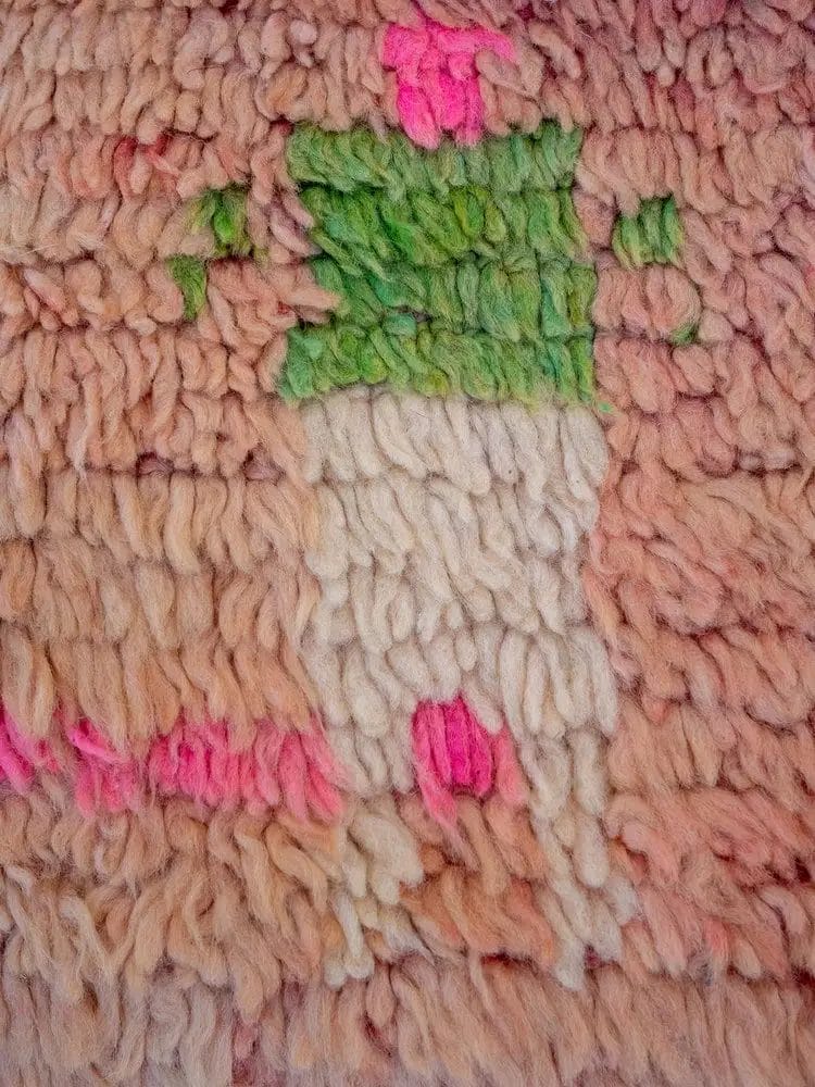 Close-up van een gestructureerde stof met daarop een eenvoudig figuur in een groen topje en een witte broek op een beige en roze achtergrond.