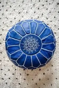 Een blauw rond kussen met wit geometrisch borduurwerk ligt op een gespikkeld grijs oppervlak.