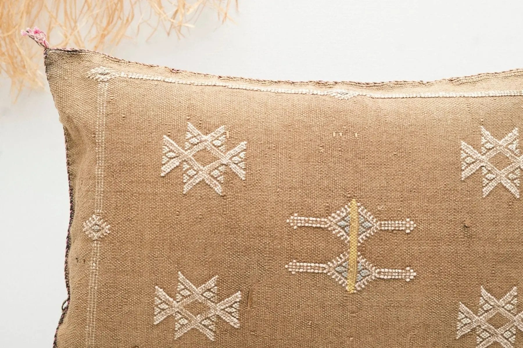 Close-up van een beige kussen met geometrisch wit borduurwerk, voorzien van ingewikkelde patronen.