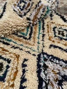 Close-up van een geweven tapijt met geometrische patronen in de kleuren crème, zwart, blauw en mosterdgeel.