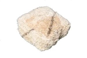 Een vierkante, zachte beige poef met een ruige textuur staat op een effen witte achtergrond.